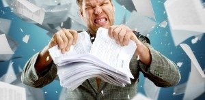 Frustrated man tearing stack of papers in half, with paperwork flying through air behind him